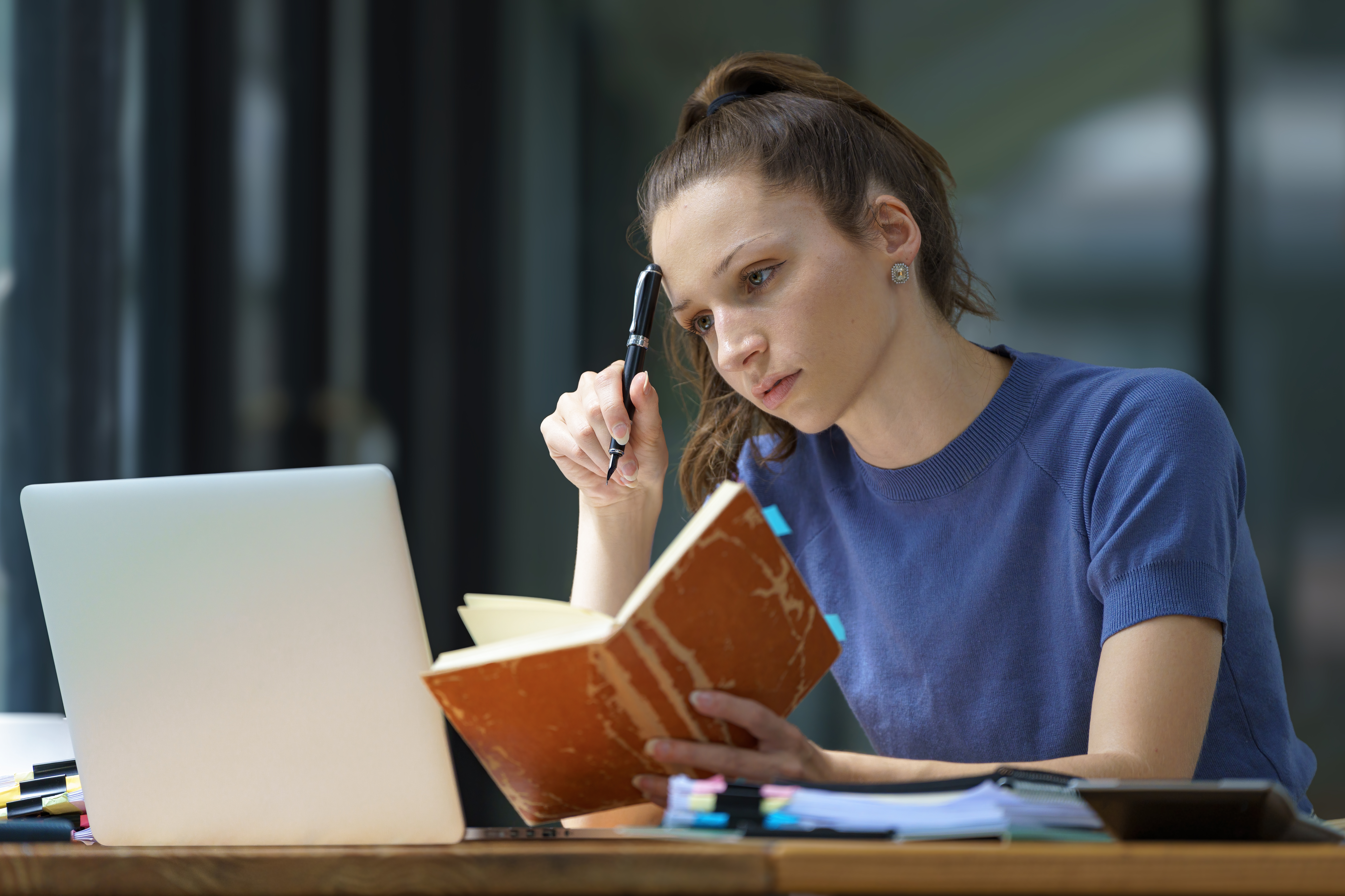 Jovem mulher estudando com um caderno e um notebook, concentrada e pensativa.