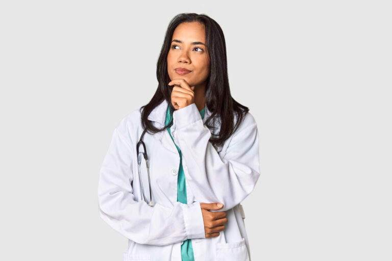 Mulher médica com expressão pensativa, vestindo jaleco branco e estetoscópio no pescoço, olhando para o lado.