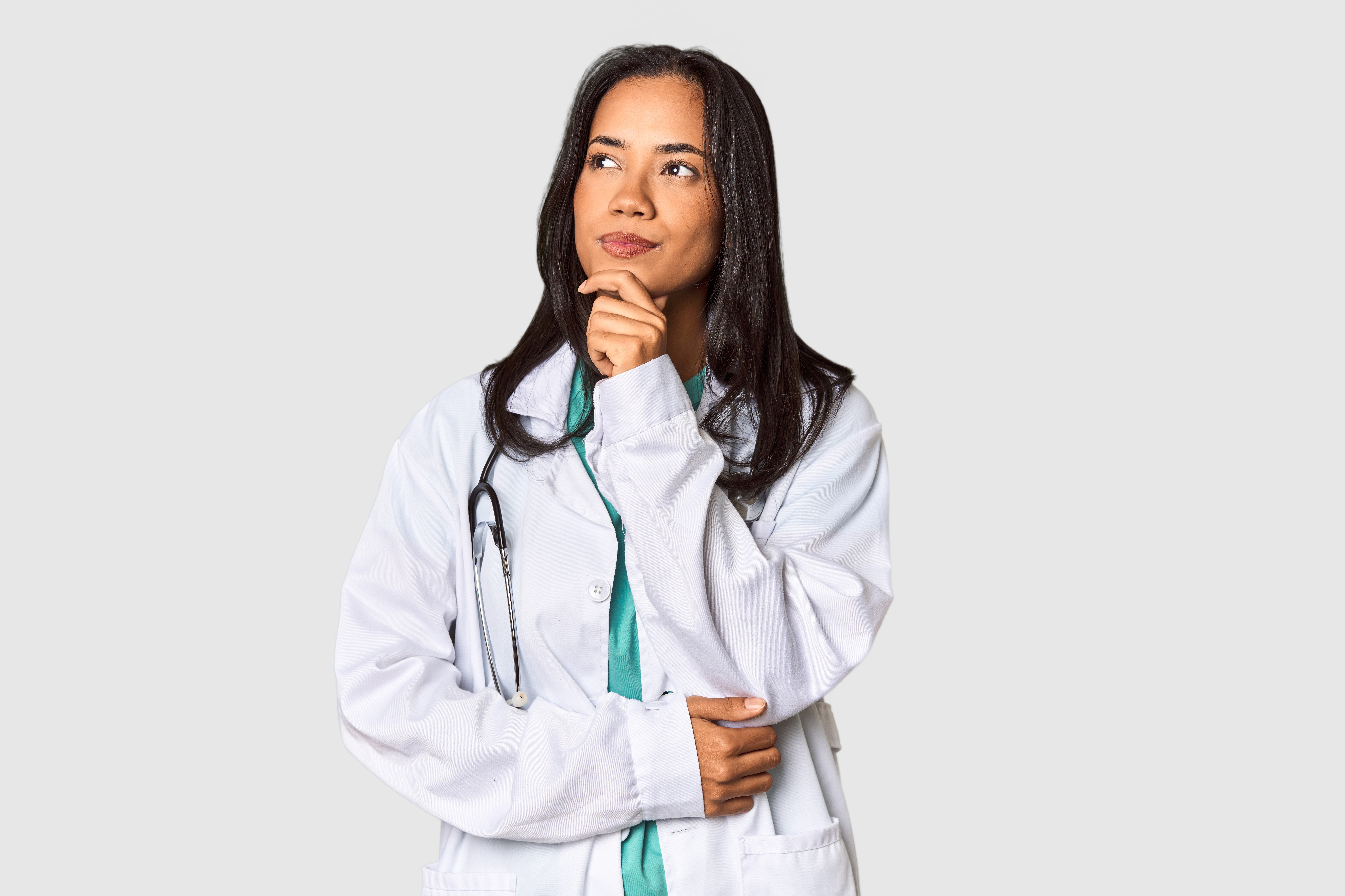 Mulher médica com expressão pensativa, vestindo jaleco branco e estetoscópio no pescoço, olhando para o lado.