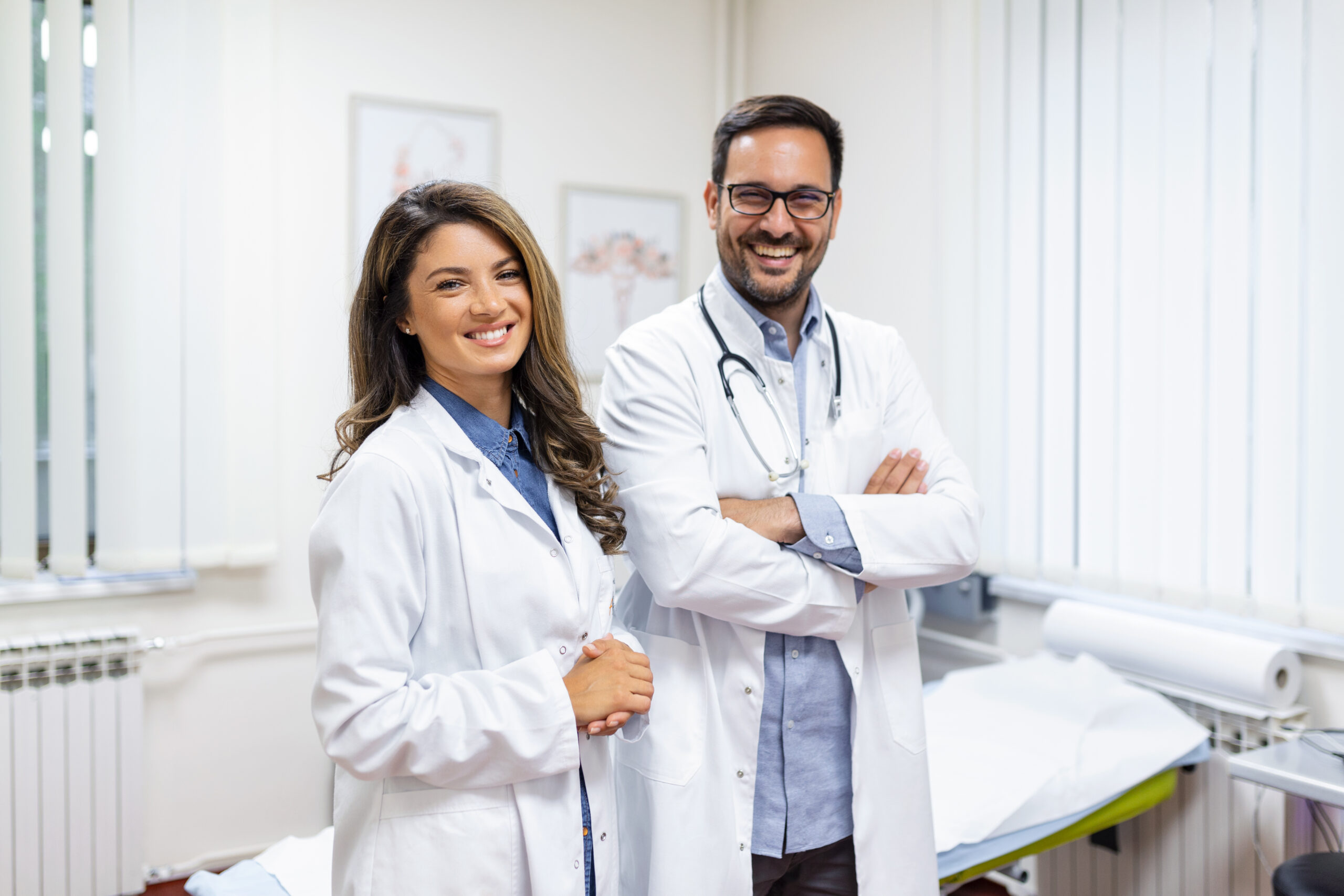 Dois jovens médicos em internato e residência médica, sorrindo e usando jalecos brancos em clínica moderna.