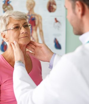 Médico examinando o pescoço de uma mulher idosa em um consultório médico.