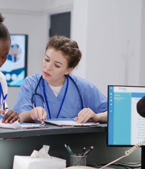 Equipe médica preenchendo formulários ao lado de recepcionista em hospital.