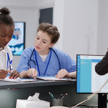 Equipe médica preenchendo formulários ao lado de recepcionista em hospital.