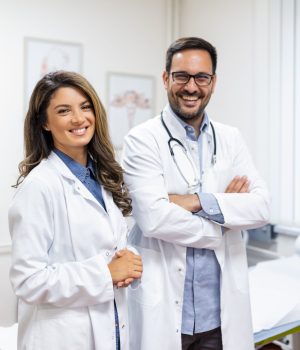 Dois jovens médicos em internato e residência médica, sorrindo e usando jalecos brancos em clínica moderna.