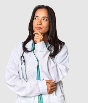 Mulher médica com expressão pensativa, vestindo jaleco branco e estetoscópio no pescoço, olhando para o lado.