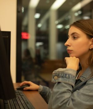 Mulher jovem concentrada utilizando um computador de mesa em ambiente interno à noite.
