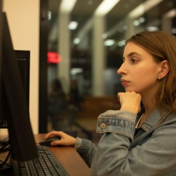 Mulher jovem concentrada utilizando um computador de mesa em ambiente interno à noite.