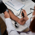 Profissional de saúde realiza a medição da pressão arterial de um paciente utilizando um esfigmomanômetro em consultório médico.