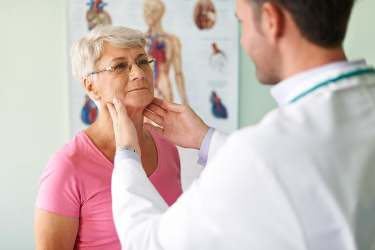 Médico examinando o pescoço de uma mulher idosa em um consultório médico.