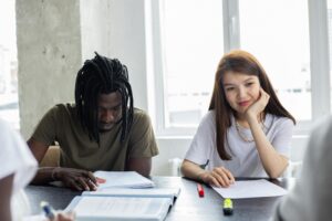 Dois estudantes sentados em uma mesa durante uma atividade em grupo, analisando anotações e materiais de estudo em uma sala iluminada.