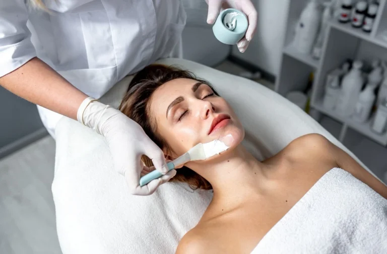 Profissional aplica máscara facial em cliente durante tratamento estético em clínica.