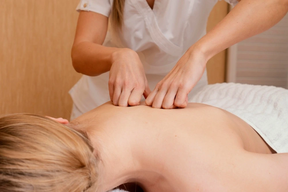 Profissional realiza massagem terapêutica nas costas de cliente deitada em maca.