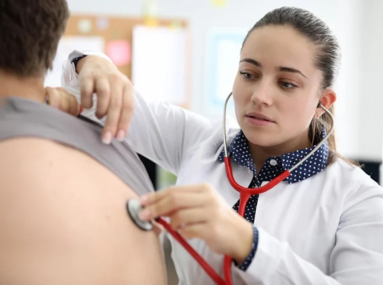Profissional de saúde examinando as costas de um paciente com um estetoscópio durante uma consulta.