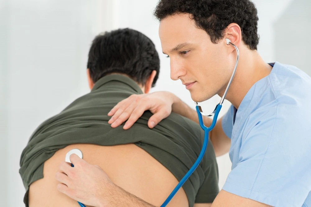 Profissional de saúde auscultando as costas de um paciente com um estetoscópio durante uma consulta.