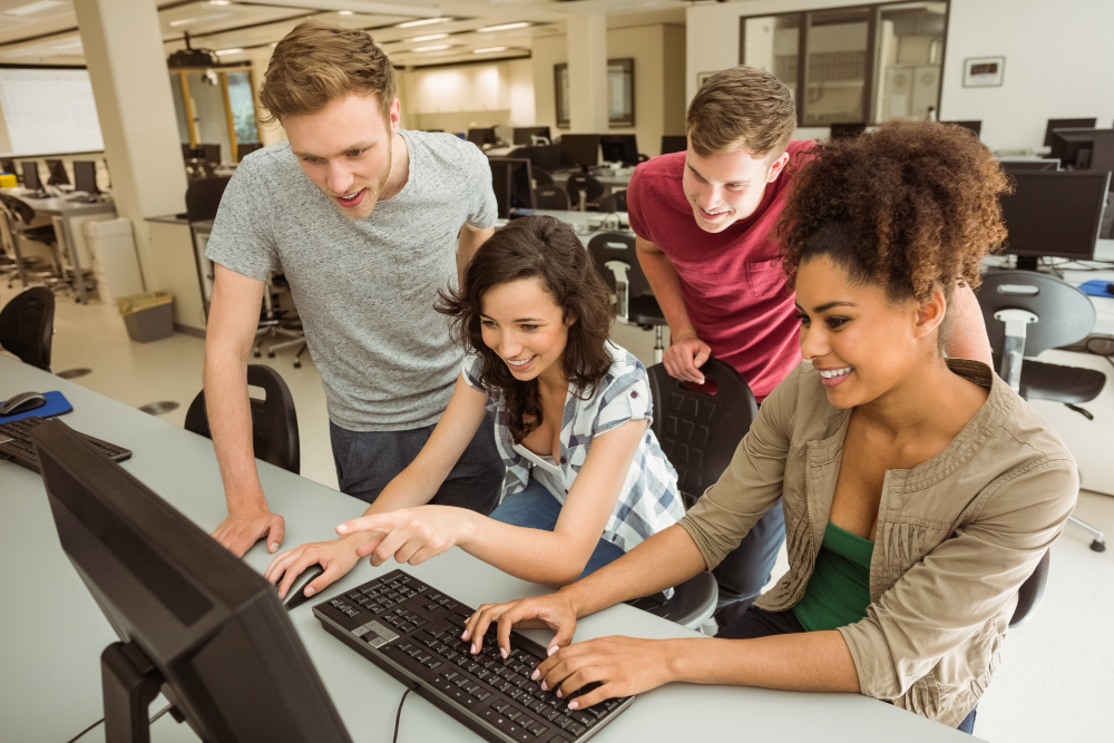 Grupo de estudantes de Ciência da Computação trabalhando juntos em frente a um computador em um laboratório de informática.