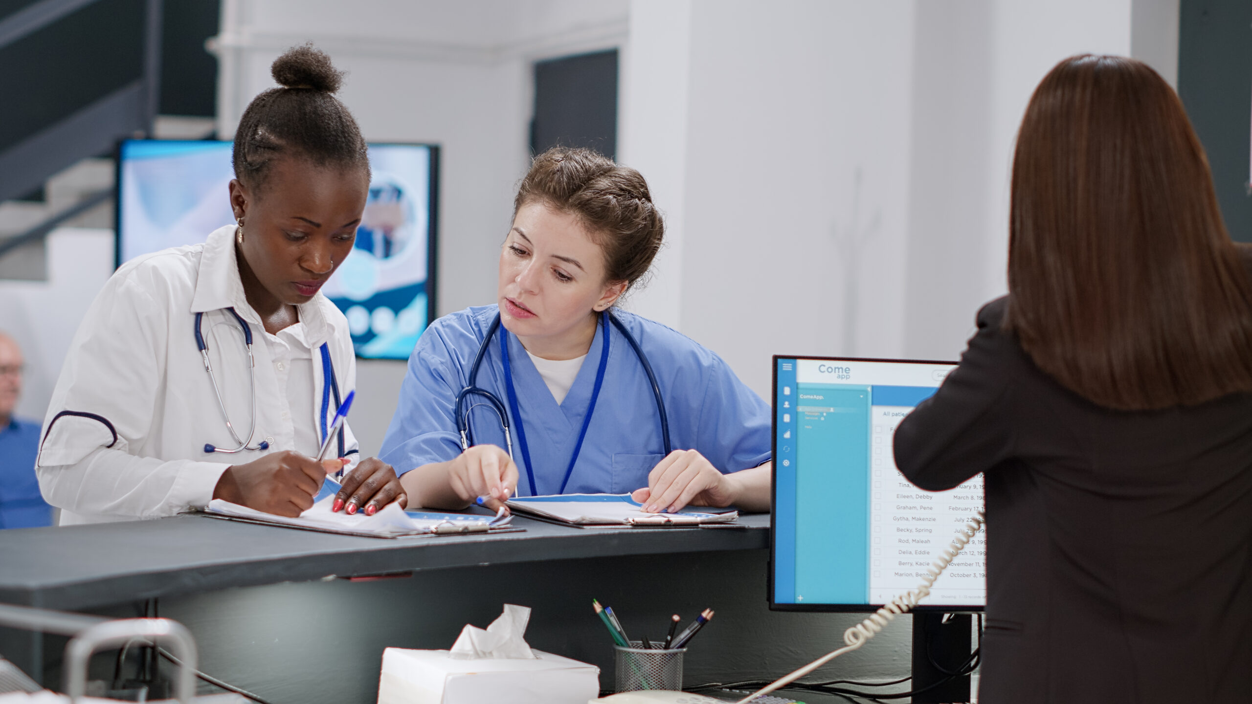 Equipe médica preenchendo formulários ao lado de recepcionista em hospital.
