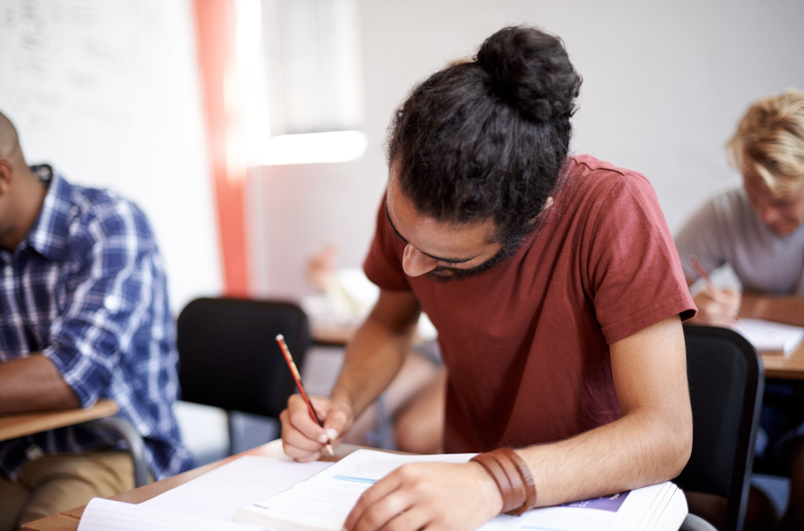 Estudante escrevendo concentrado em sala de aula.