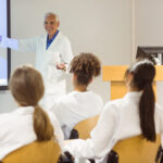 Professor de medicina explicando conteúdo em sala de aula para alunos com jaleco