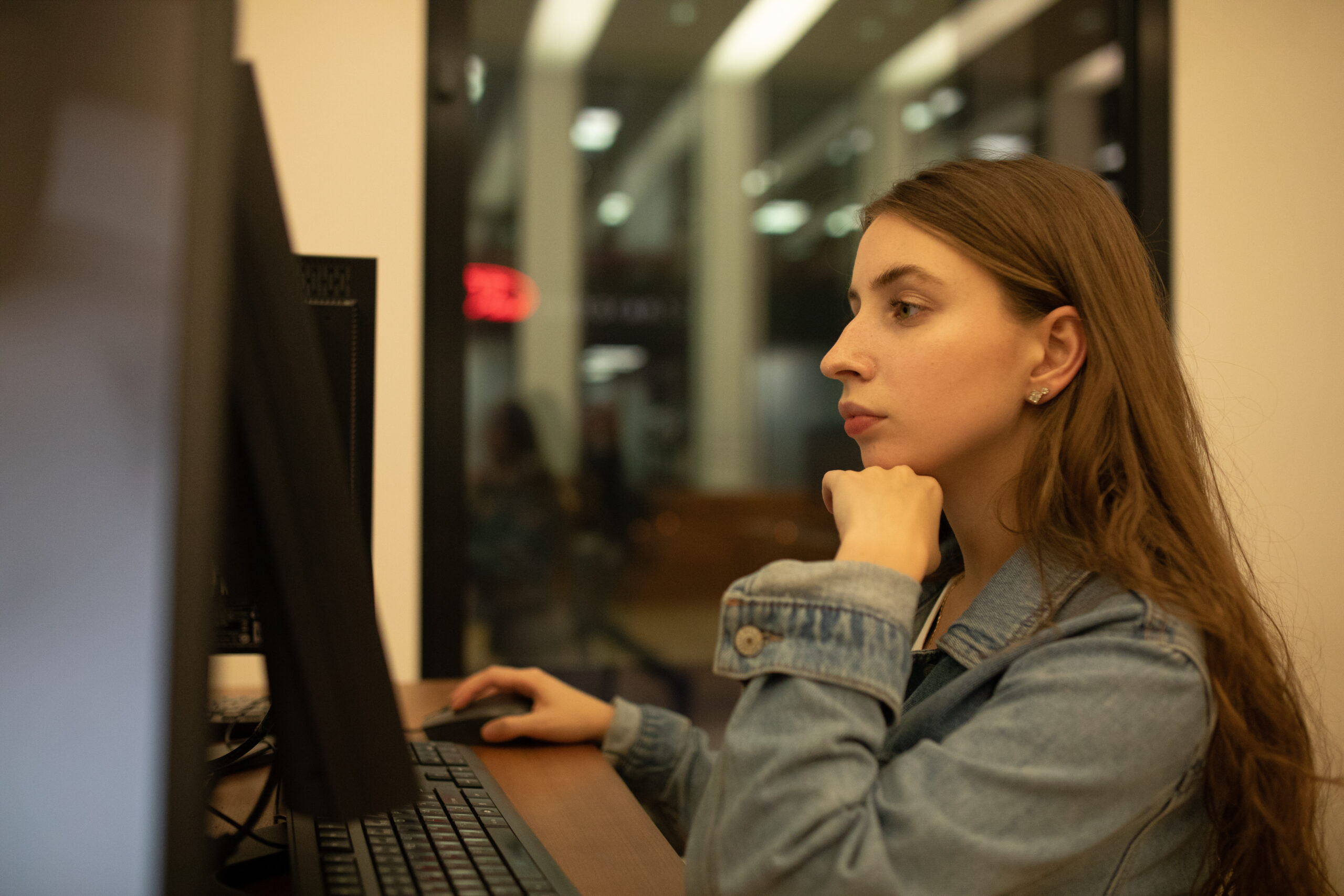 Mulher jovem concentrada utilizando um computador de mesa em ambiente interno à noite.